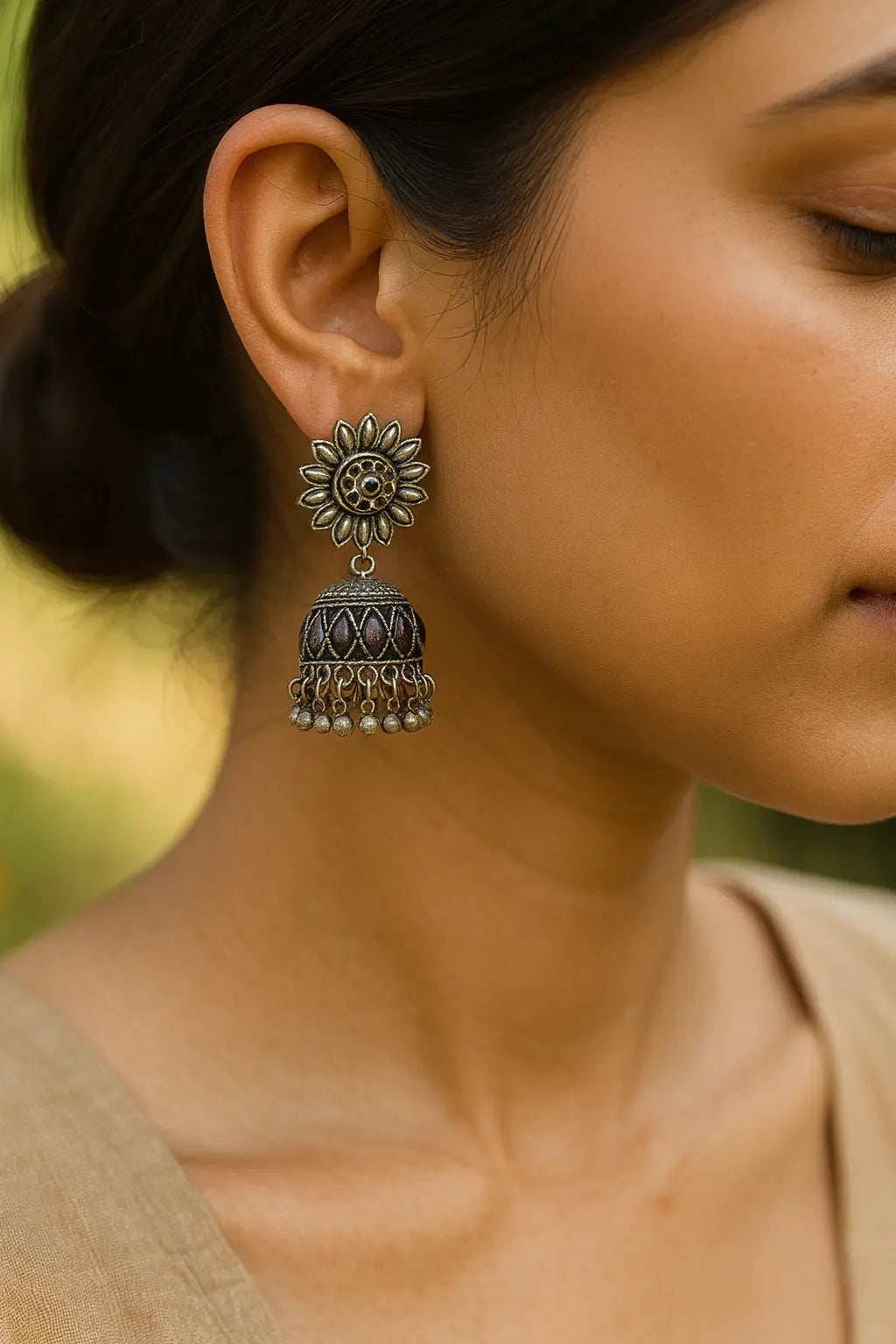 Close-up of a woman wearing oxidised silver Aakriti Jhumka earrings with floral stud design and detailed dome pattern, photographed outdoors in natural light.