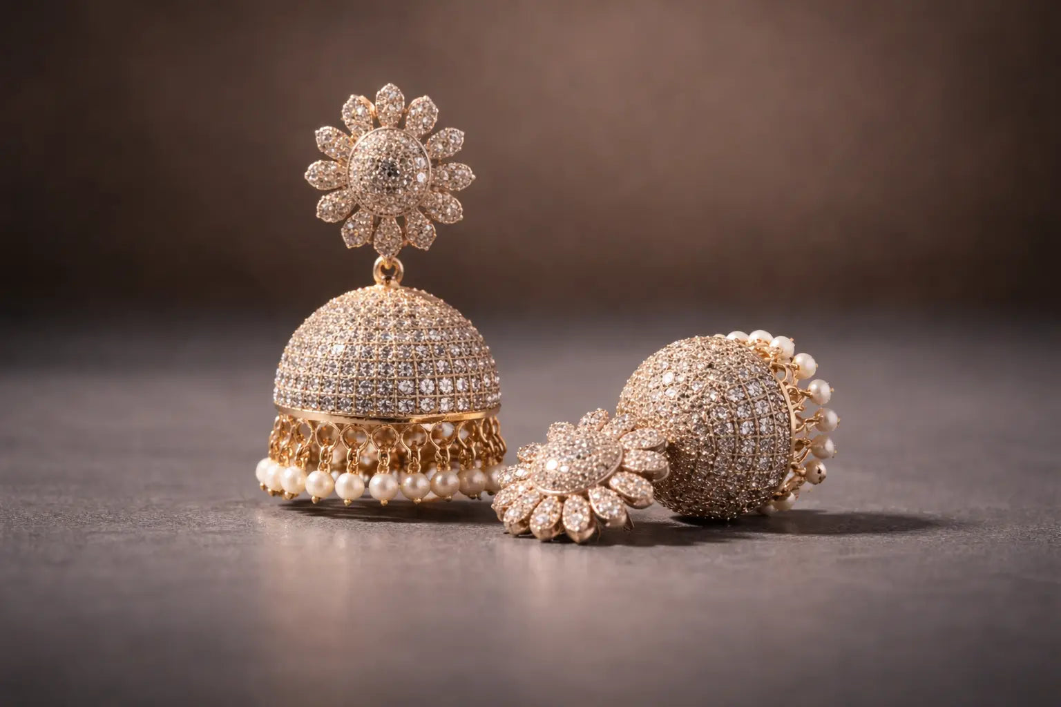 Close-up landscape image of gold-plated diamond jhumka earrings with pearl detailing, featuring floral stud design and pavé stone work – premium traditional jewellery for women