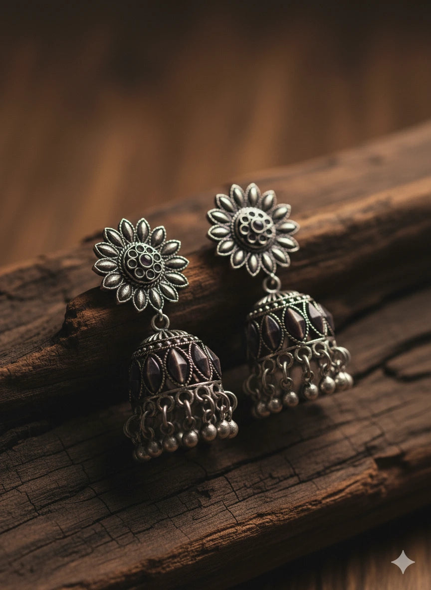 Silver floral earrings on a wooden surface. Close-up of Shinora Aakriti Jhumka – handcrafted oxidized silver earrings with detailed filigree work and ghungroo drops from Shinora