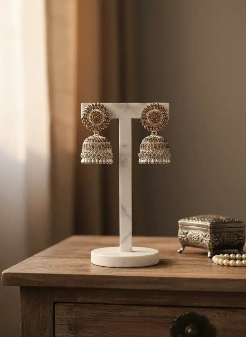 Dia Jhumka – gold-tone double-dome jhumka earrings with sunburst stud and brown CZ stones displayed on a white marble stand from Shinora