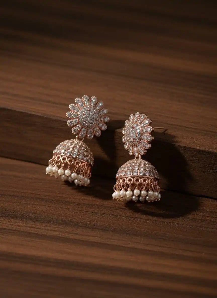 Noor Jhumka – rose-gold diamond jhumka earrings with intricate floral stud design placed on a wooden surface from Shinora