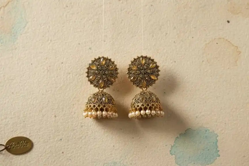Heer Jhumka – gold-tone floral jhumka earrings with pearl drops hanging on textured beige background from Shinora