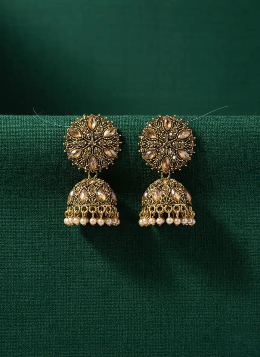 Heer Jhumka – antique gold floral jhumka earrings displayed on green fabric, traditional ethnic jewelry design.