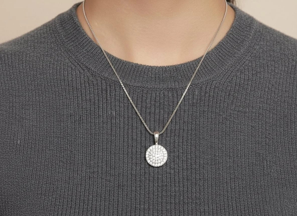 Close-up of The Celeste Necklace with sparkling round crystal pendant and silver chain, styled over a grey textured sweater by shinora