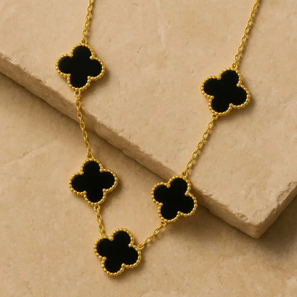 Gold clover necklace with black enamel charms displayed on beige stone background for premium jewelry photography from shinora