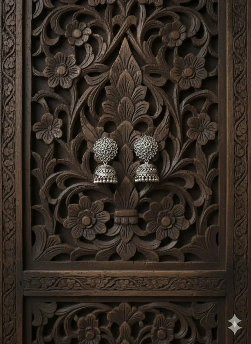 Oxidised silver jhumka earrings displayed on an intricately carved wooden floral backdrop highlighting their traditional design from Shinora