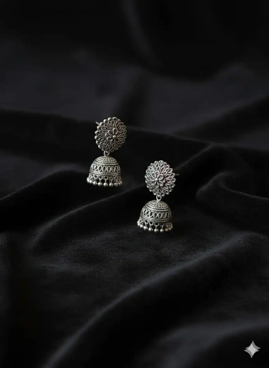 Pair of oxidised silver jhumka earrings placed on soft black velvet fabric, emphasizing their detailed filigree work from Shinora