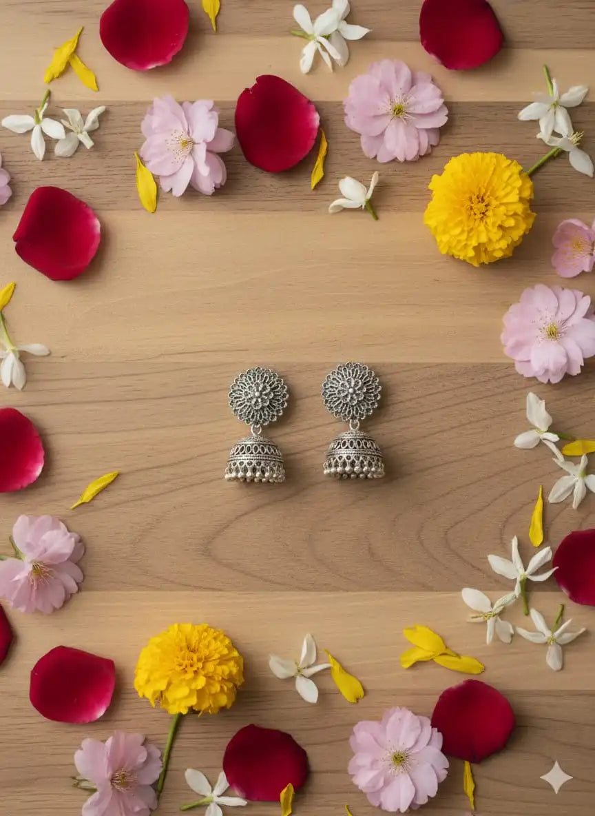 Oxidised silver jhumka earrings styled on a wooden surface surrounded by colorful flower petals for an aesthetic festive look from Shinora