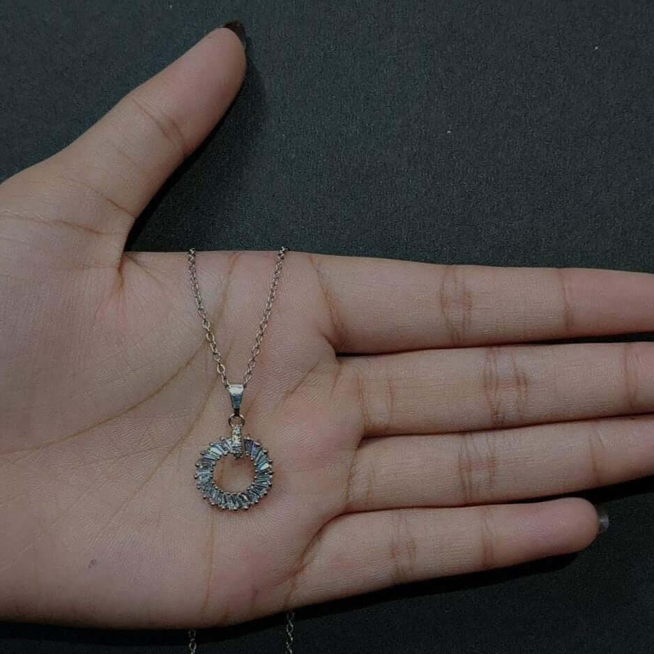 Silver necklace with a circular pendant held in a hand against a dark background